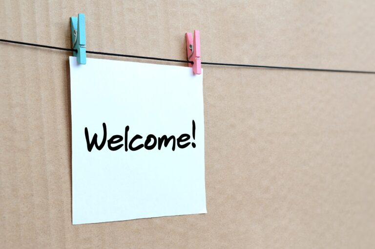 Welcome! Note is written on a white sticker that hangs with a clothespin on a rope on a background of brown cardboard